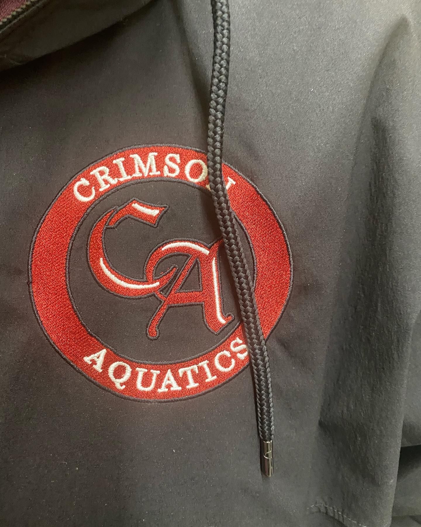 Black jacket with Crimson Aquatics logo: red circle with white 