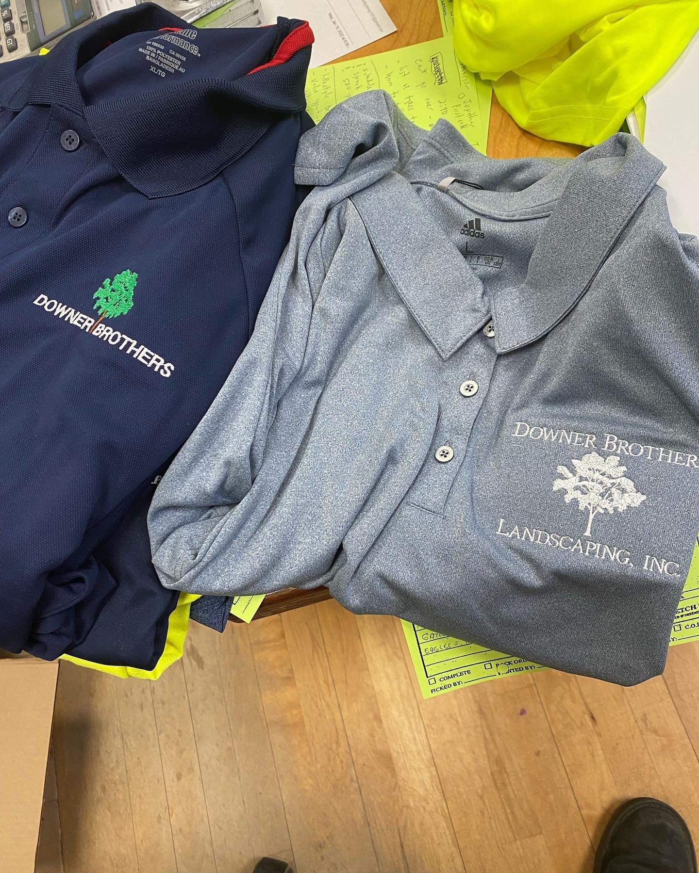 Two work shirts: one navy, one gray. Both have company logos on the chest, on a wooden table.