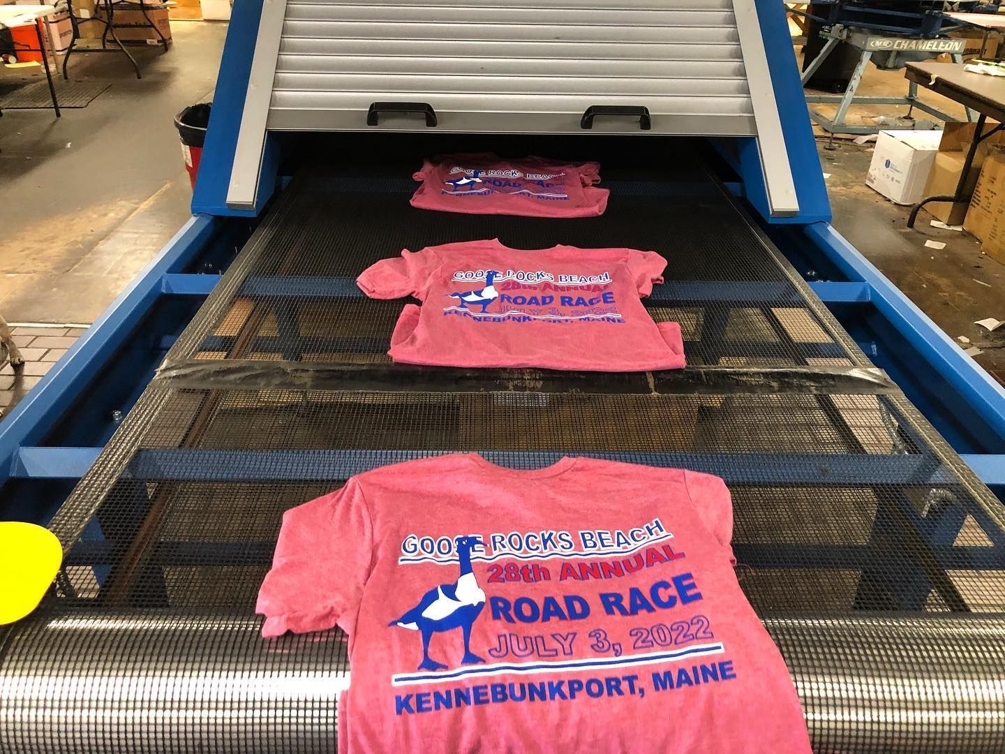 Pink t-shirts with printed design on a conveyor belt, drying in a machine.