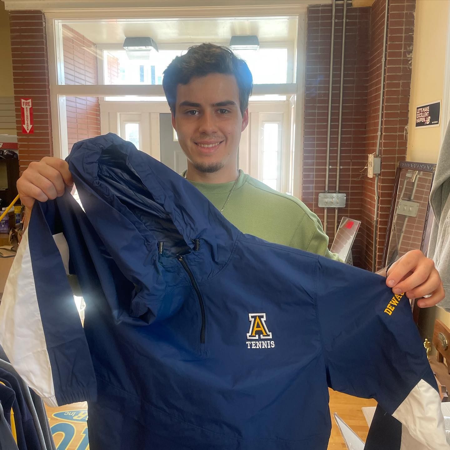 Person holding a navy and white jacket with a school logo; inside a building.