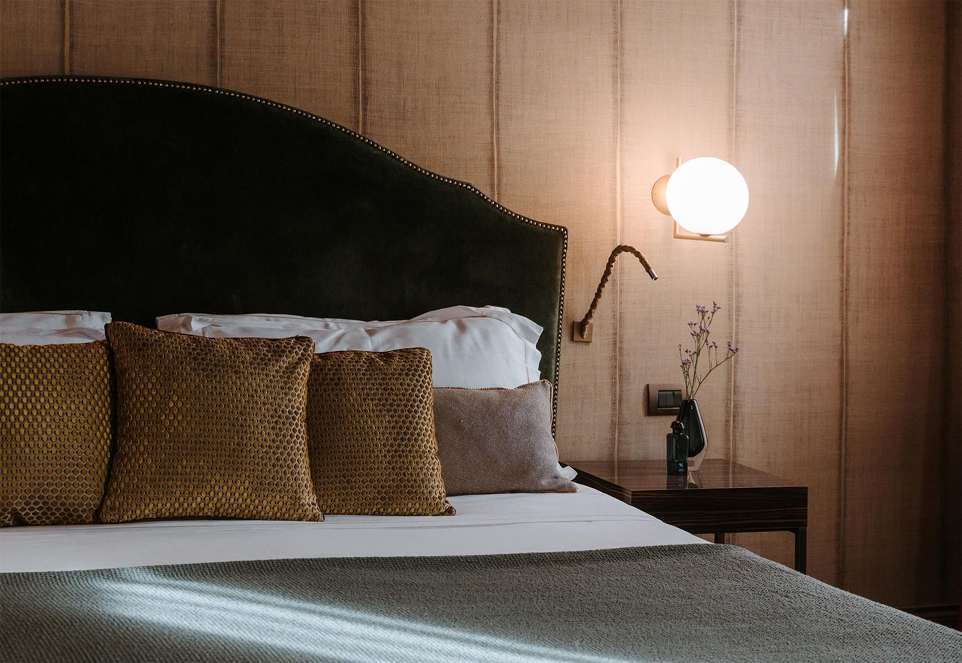 Cozy bed with dark green headboard, brown pillows, and a lit bedside lamp in a warm-toned bedroom