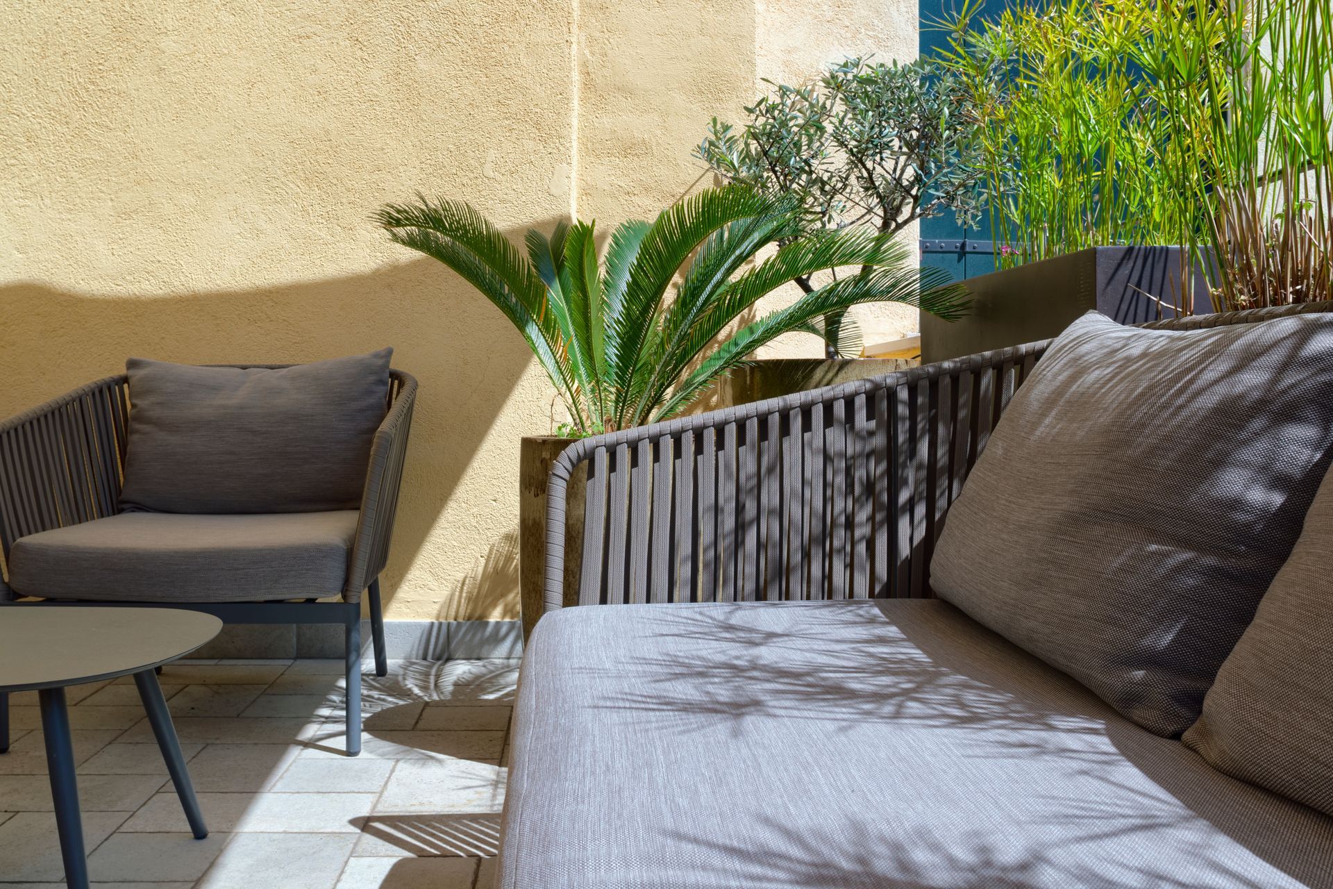 Outdoor patio with wicker seating, cream cushions, and a large beige umbrella in a courtyard garden