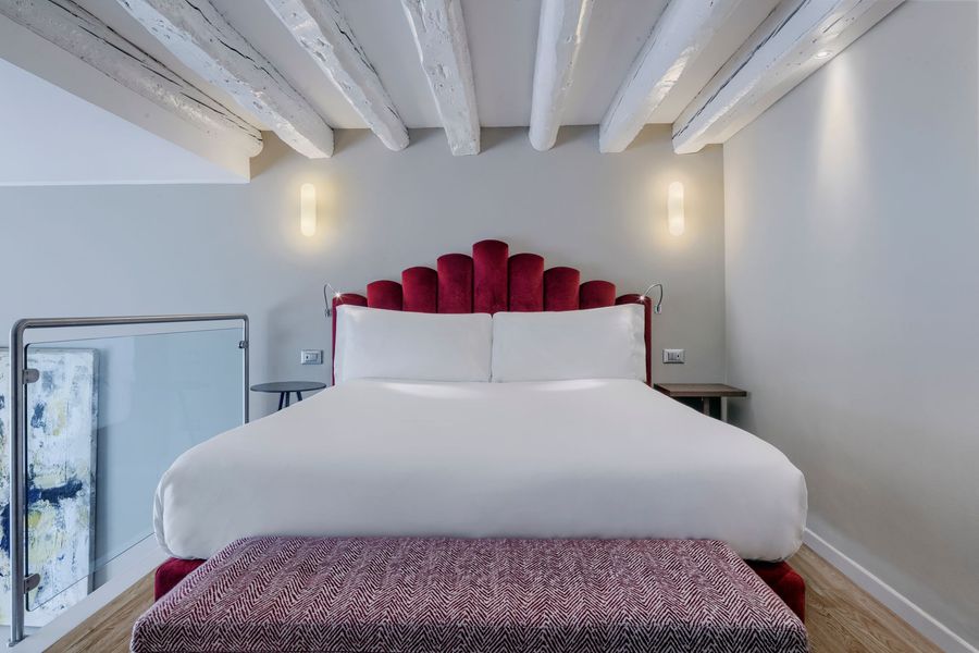 Camera da letto moderna grigia con testiera alta imbottita, panca bassa e lampade da comodino.