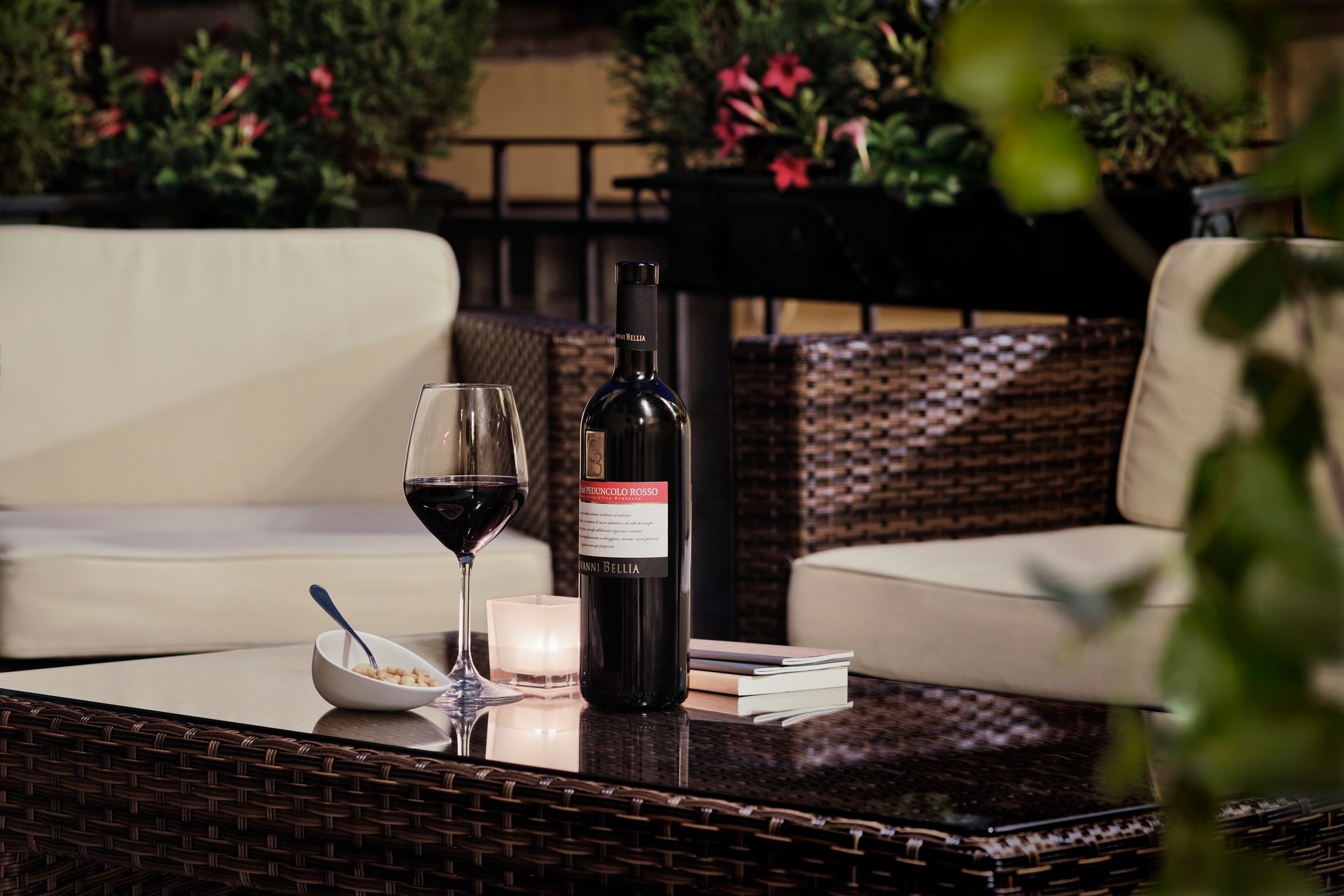 Du vin et une bougie sur une table basse en osier à côté de chaises de patio blanches dans un salon de jardin confortable.
