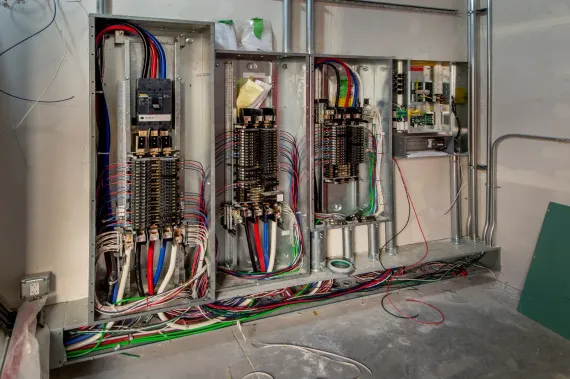 Electrical panels with wires in an unfinished room.