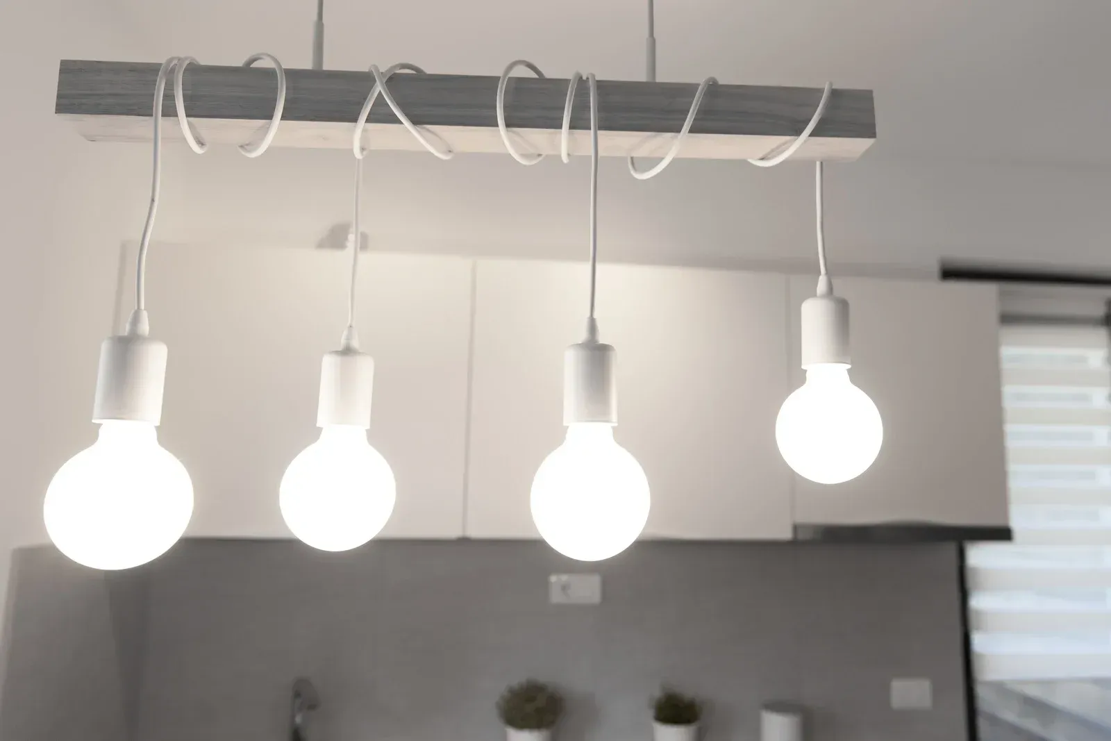 Four bright light bulbs hanging from a wooden beam in a kitchen.