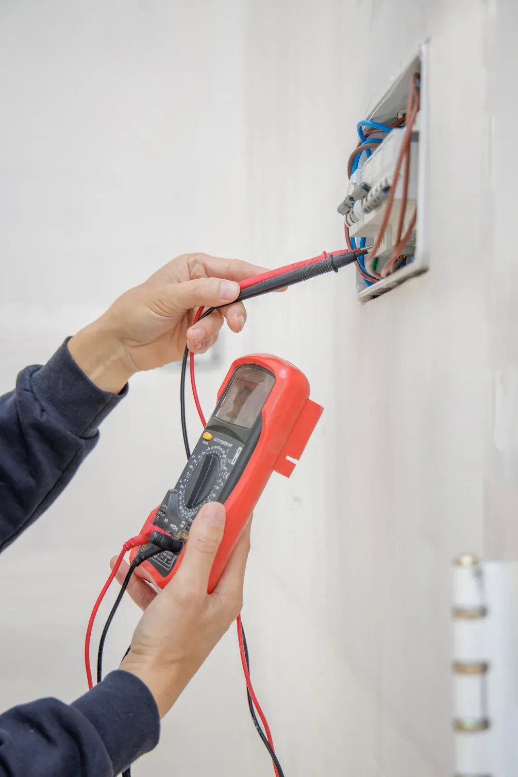 Hands wearing gloves using a multimeter to test a laptop circuit board.