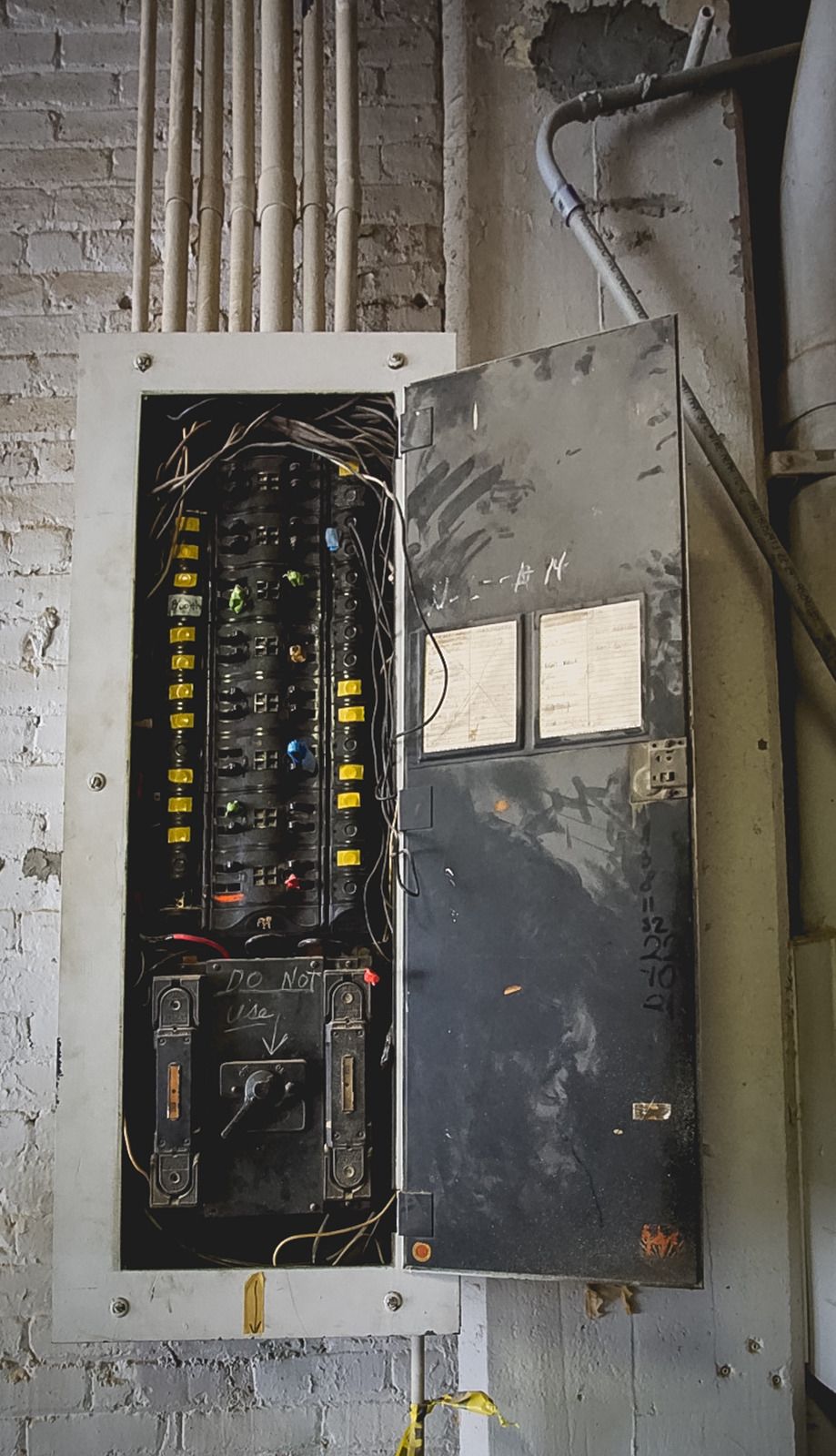 Electrical panel with open door, mounted on a brick wall. Wires and circuit breakers are visible.