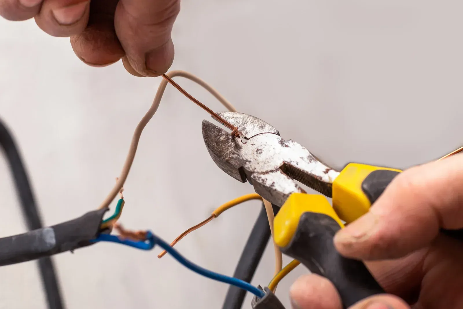 Person using a power tool to cut drywall around electrical switches.