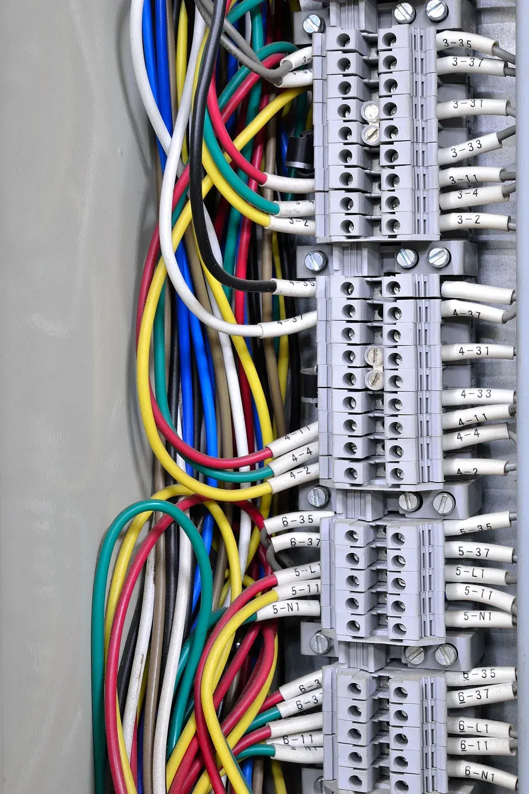 Close-up of colorful electrical wires connected to grey terminal blocks inside a panel.
