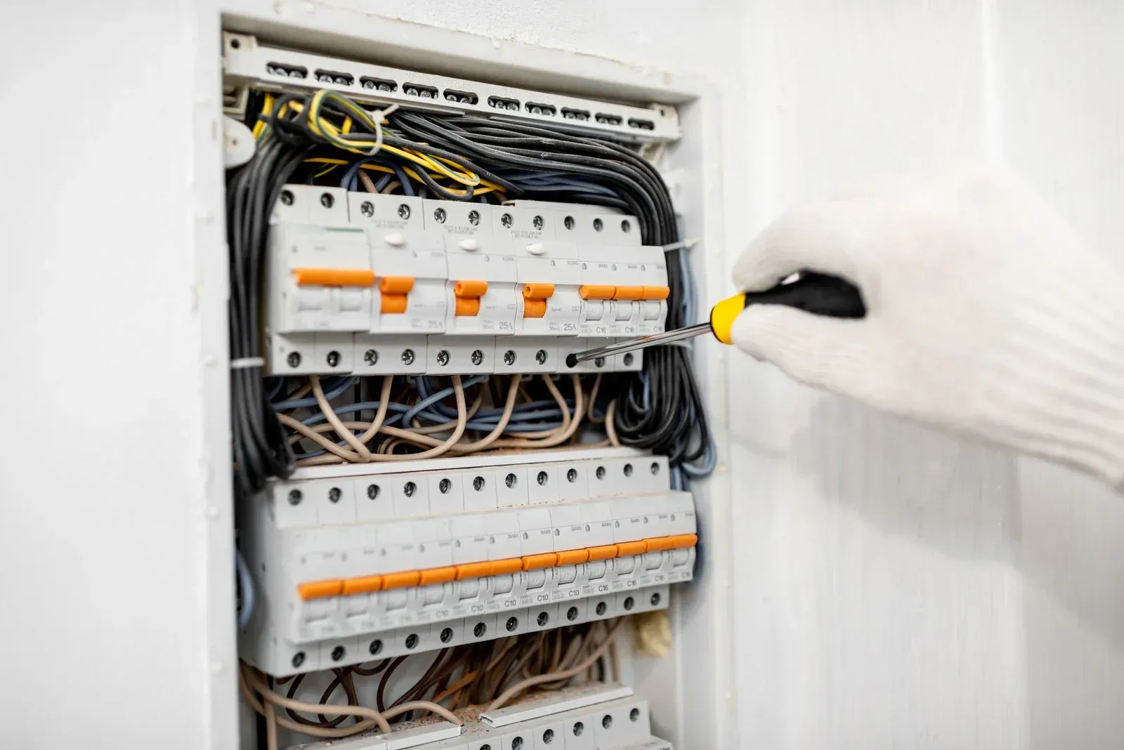 Person wearing white glove using screwdriver on electrical panel.