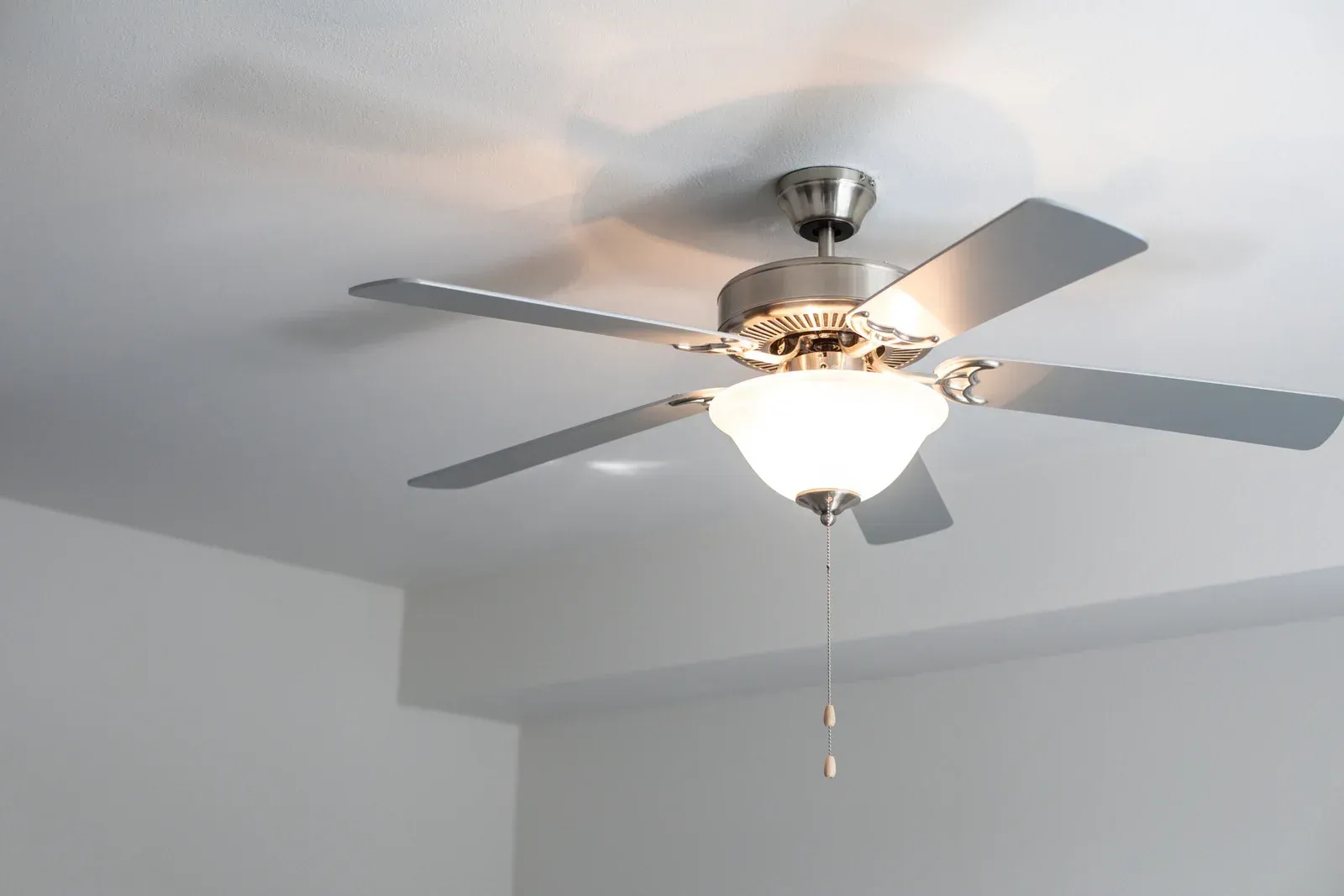 Ceiling fan with five silver blades and a light fixture, mounted on a white ceiling.