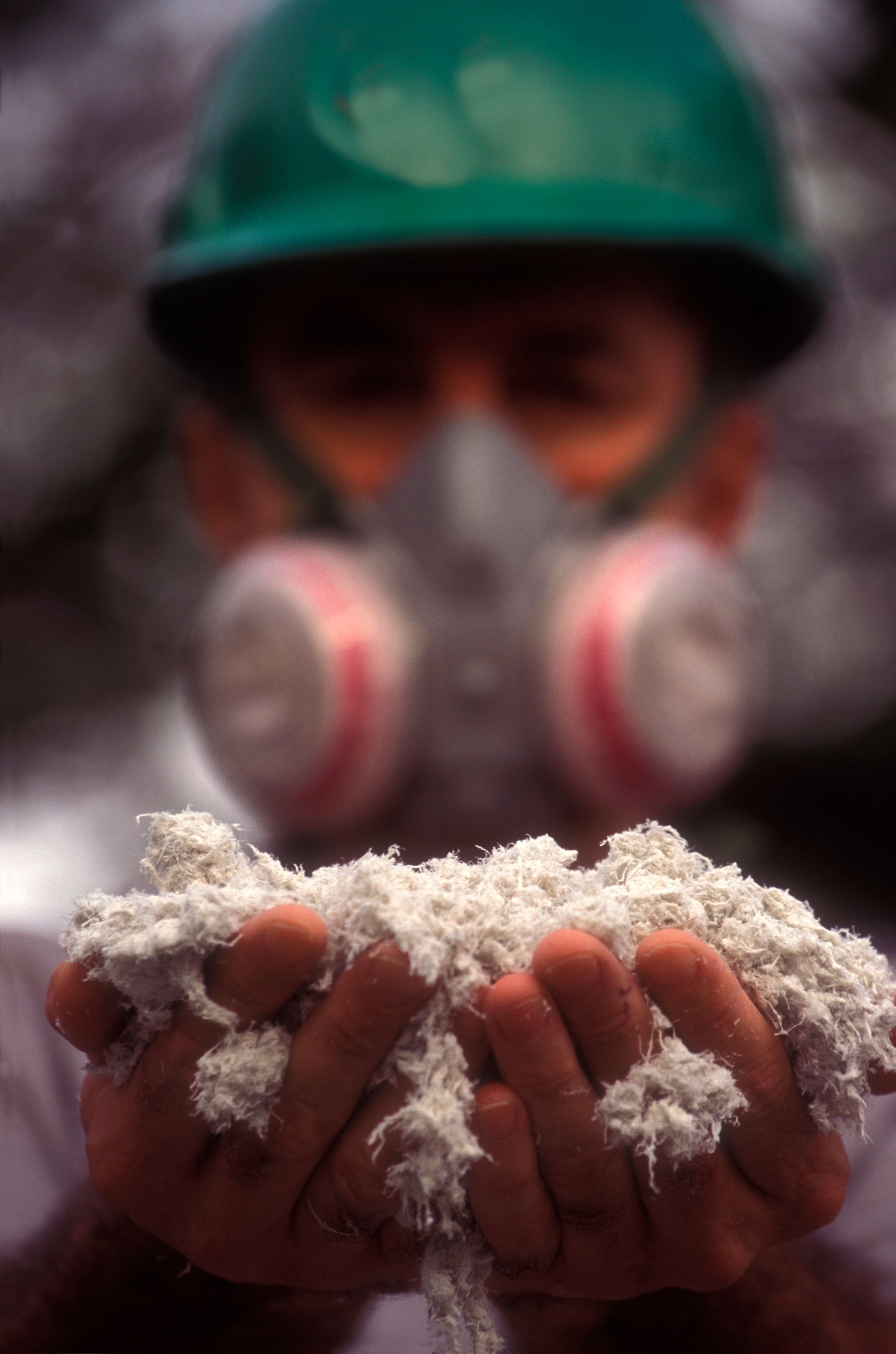 Worker in safety gear holding hazardous asbestos fibers in protective hands.