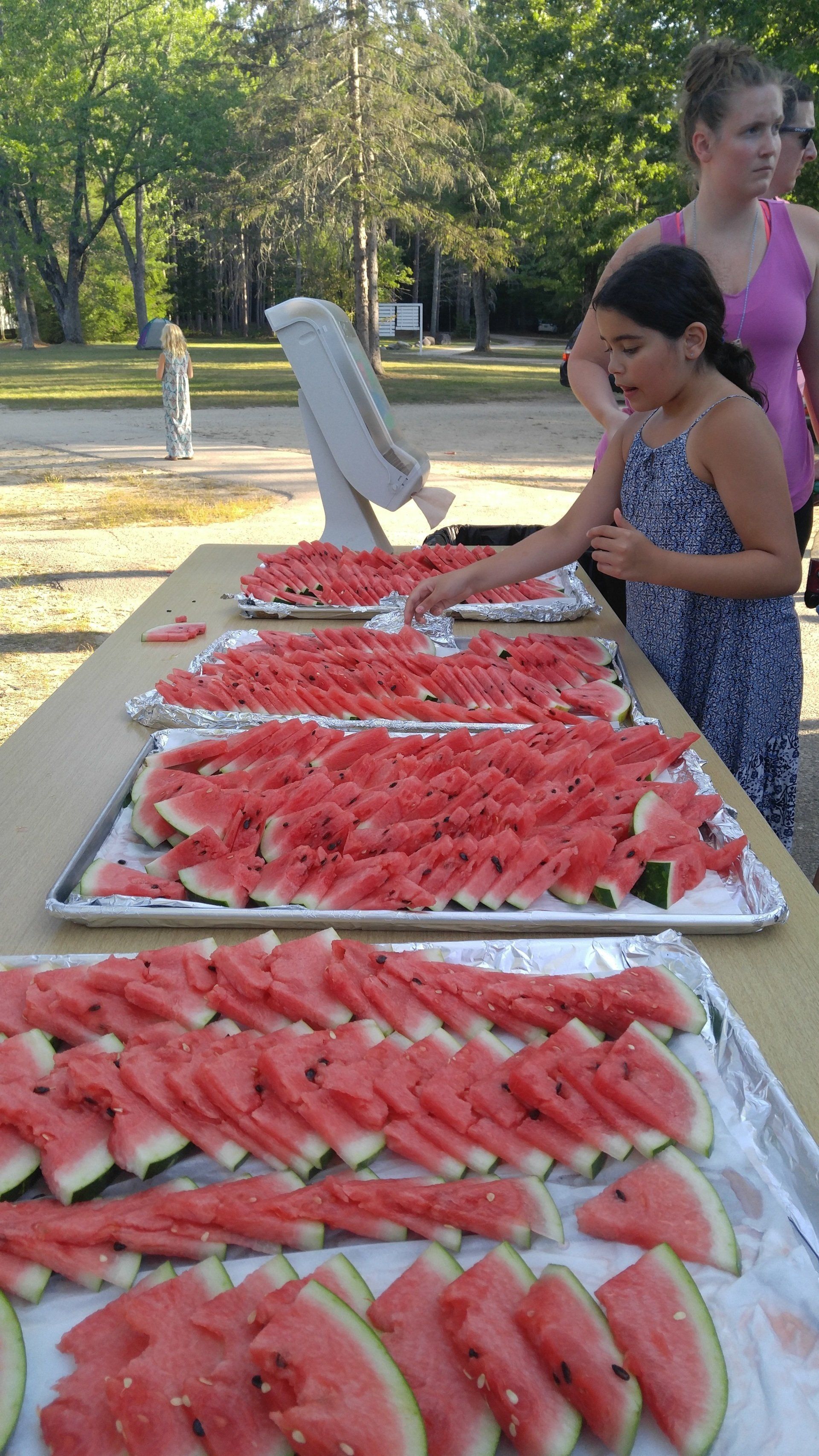 A girl is reaching for a tray of watermelon slices on a table.