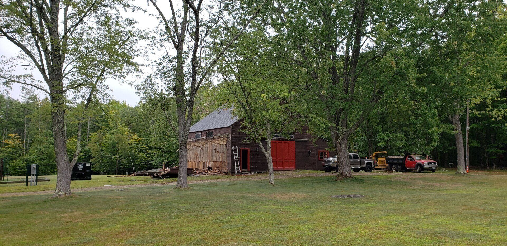 A barn with a red door is surrounded by trees in a field.