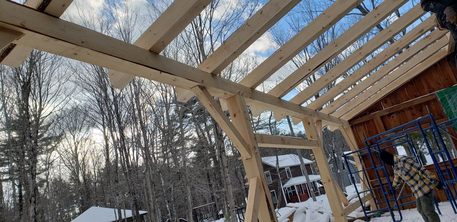 A wooden structure is being built in the snow with trees in the background.