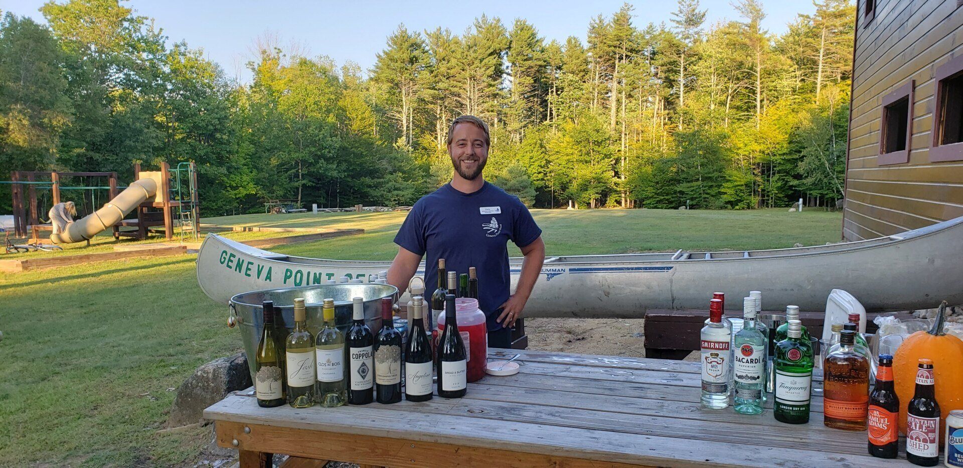 A man is standing in front of a table filled with bottles of alcohol.