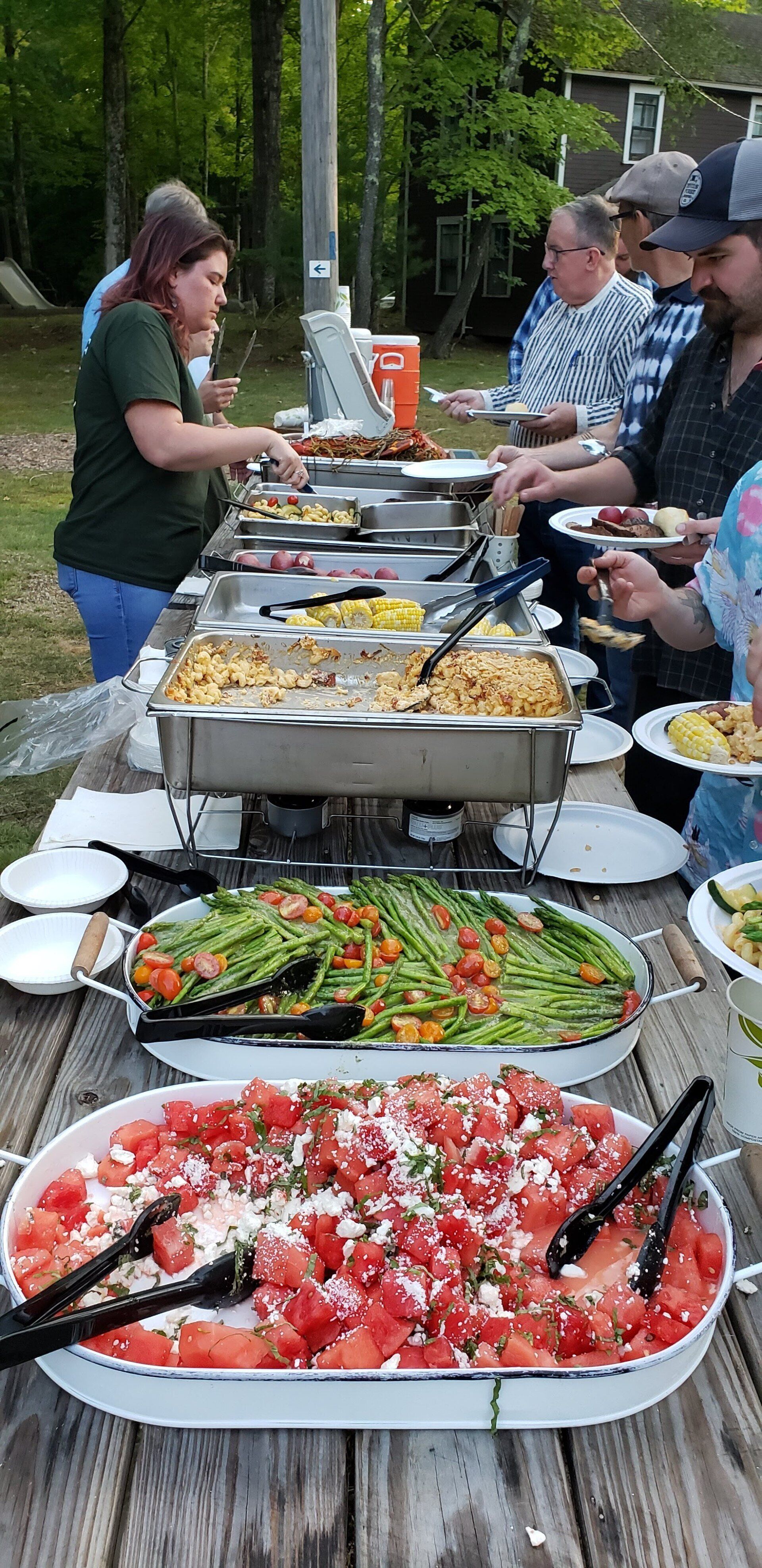 A group of people are standing around a picnic table eating food.