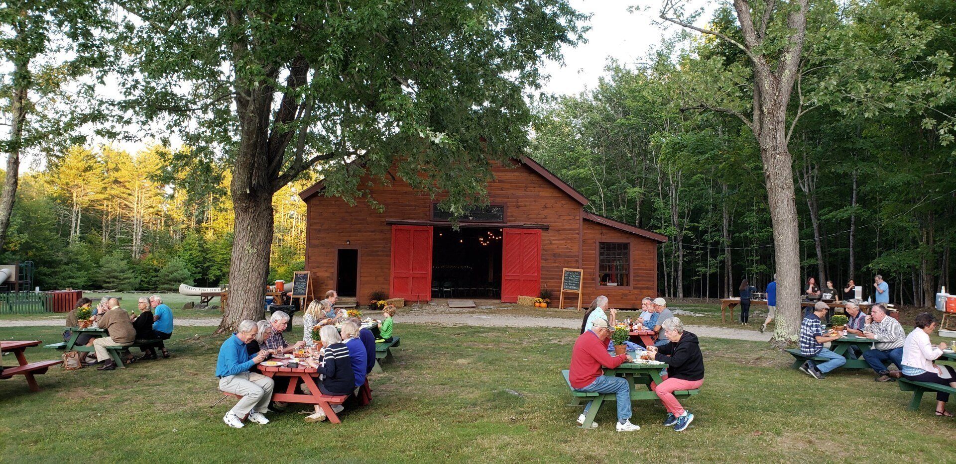 A group of people are sitting at picnic tables in front of a barn.