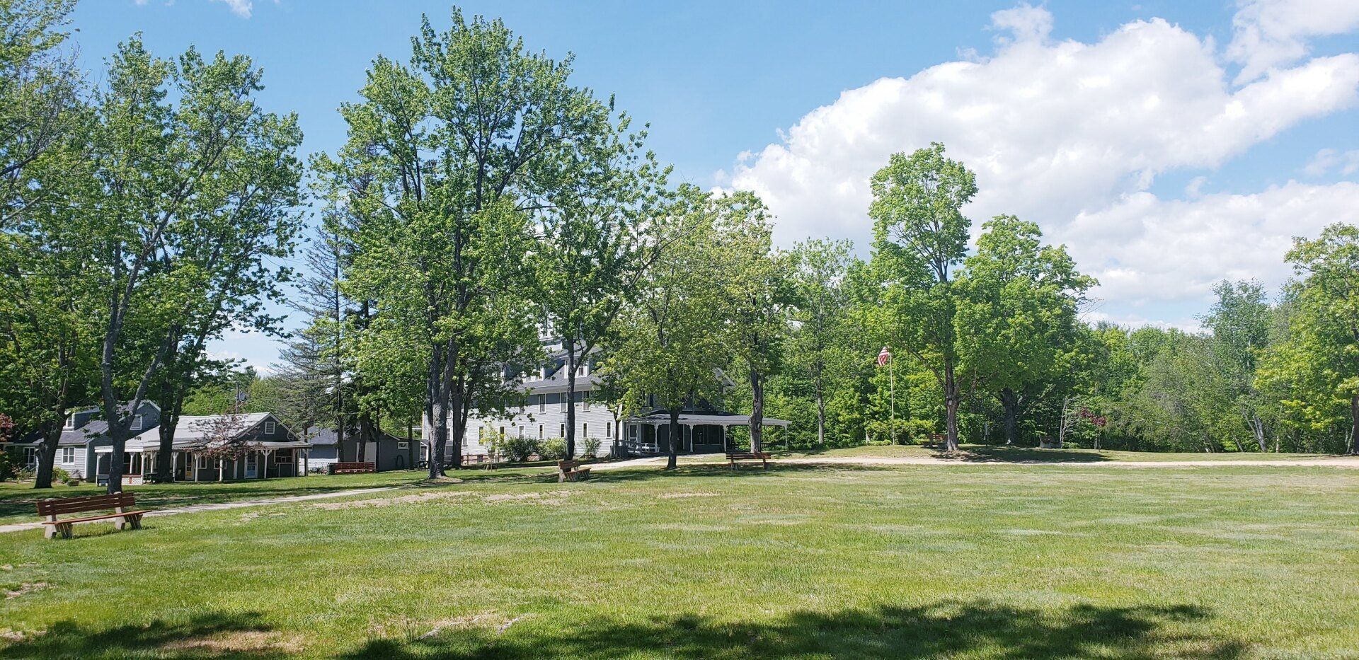 A large grassy field with trees in the background and a house in the background.