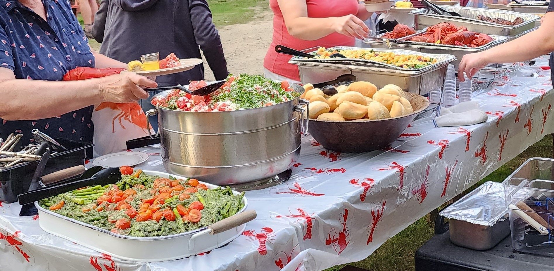 A group of people are standing around a long table filled with food.