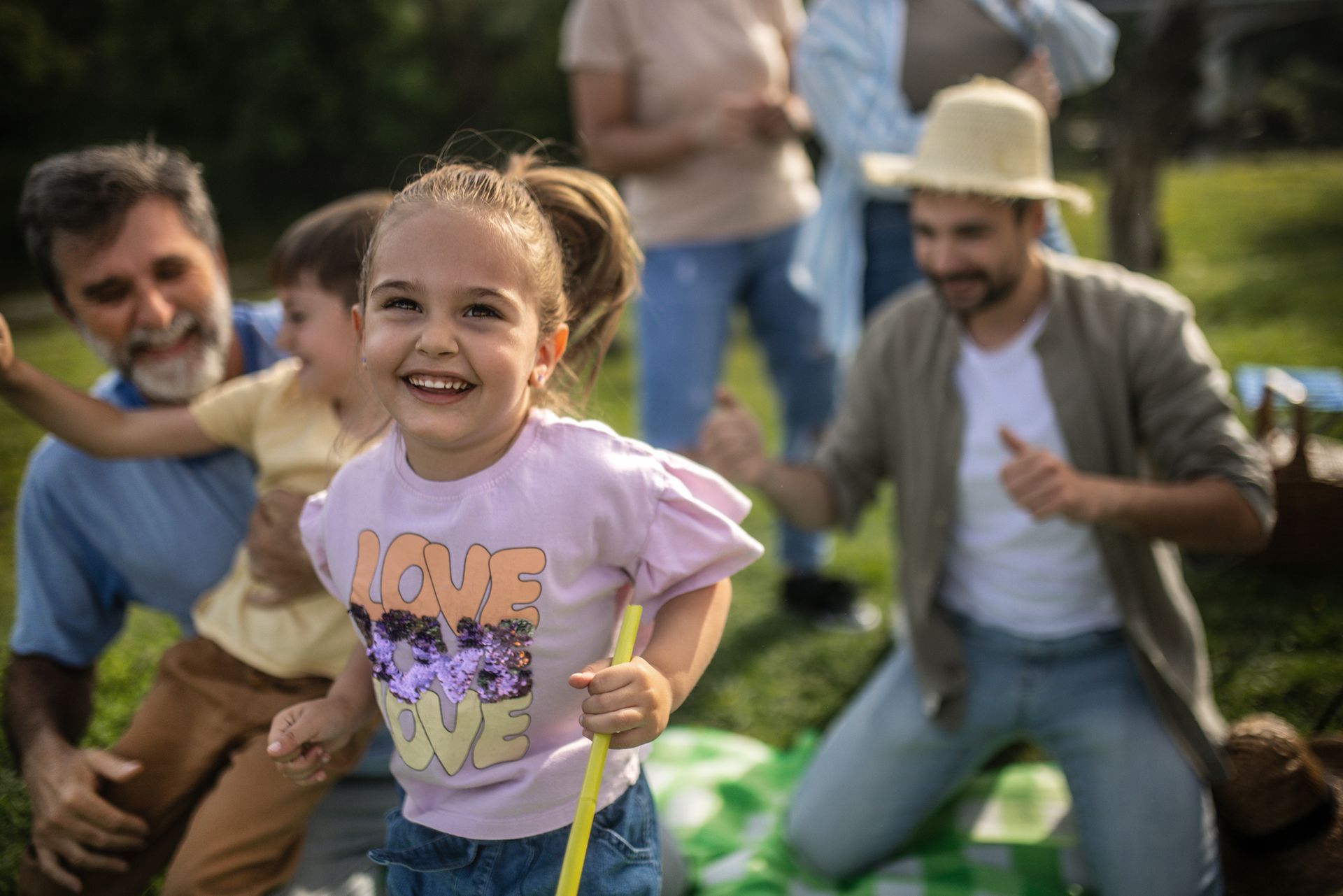 A little girl is playing with a stick in a park with her family.