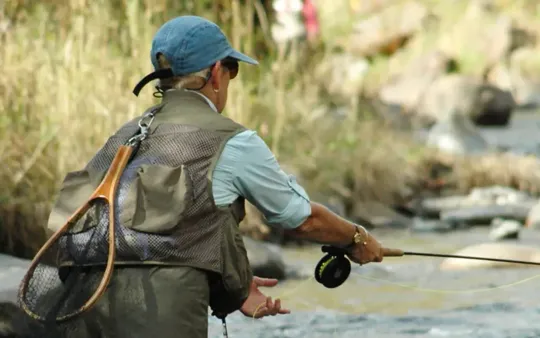 A man is fishing in a river with a fishing rod.