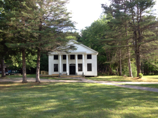 A large white house is surrounded by trees and grass