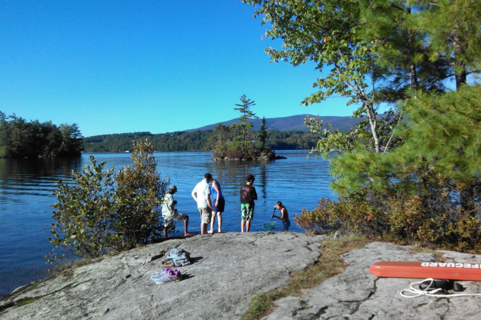 A group of people are standing on a rock near a lake.