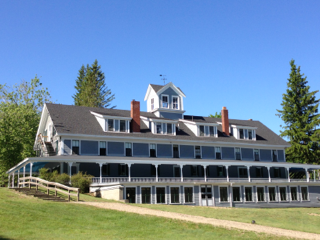 A large house sits on top of a grassy hill