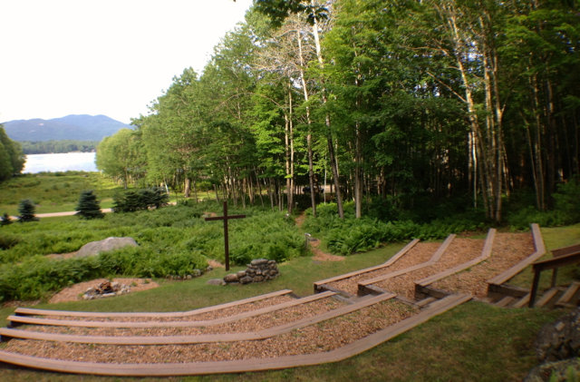 A wooden amphitheater in the middle of a forest with a lake in the background.