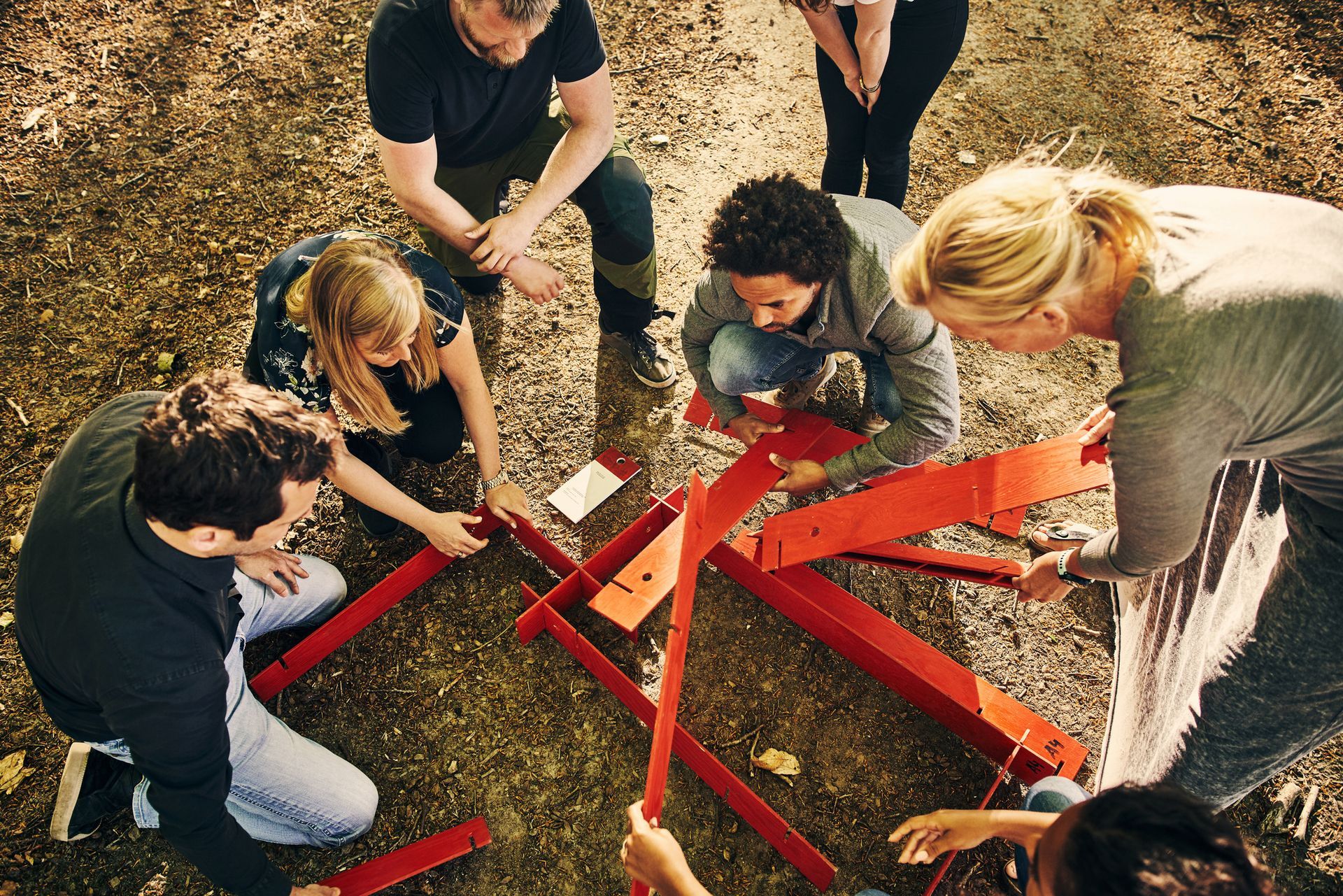 Group of people building a red structure outdoors on a grassy surface.