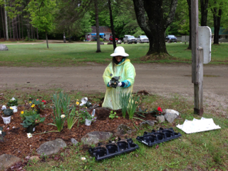 A woman in a yellow raincoat is planting flowers in a garden.