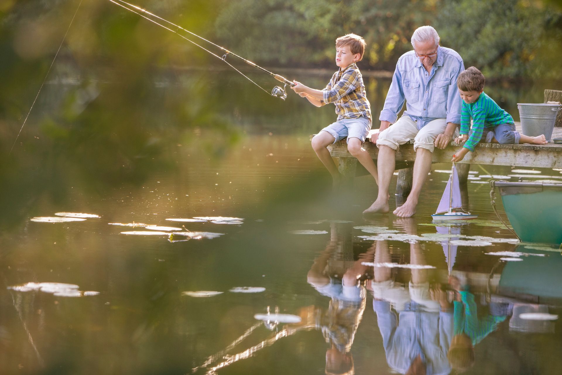 An elderly man and two young boys are fishing on a lake