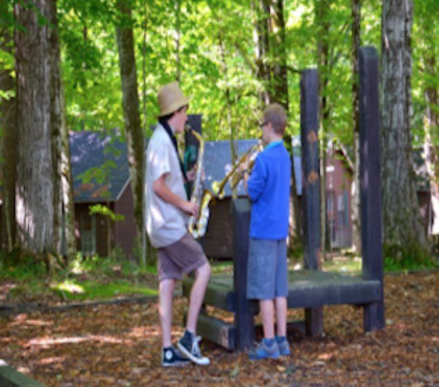 Two young boys are playing saxophones in the woods