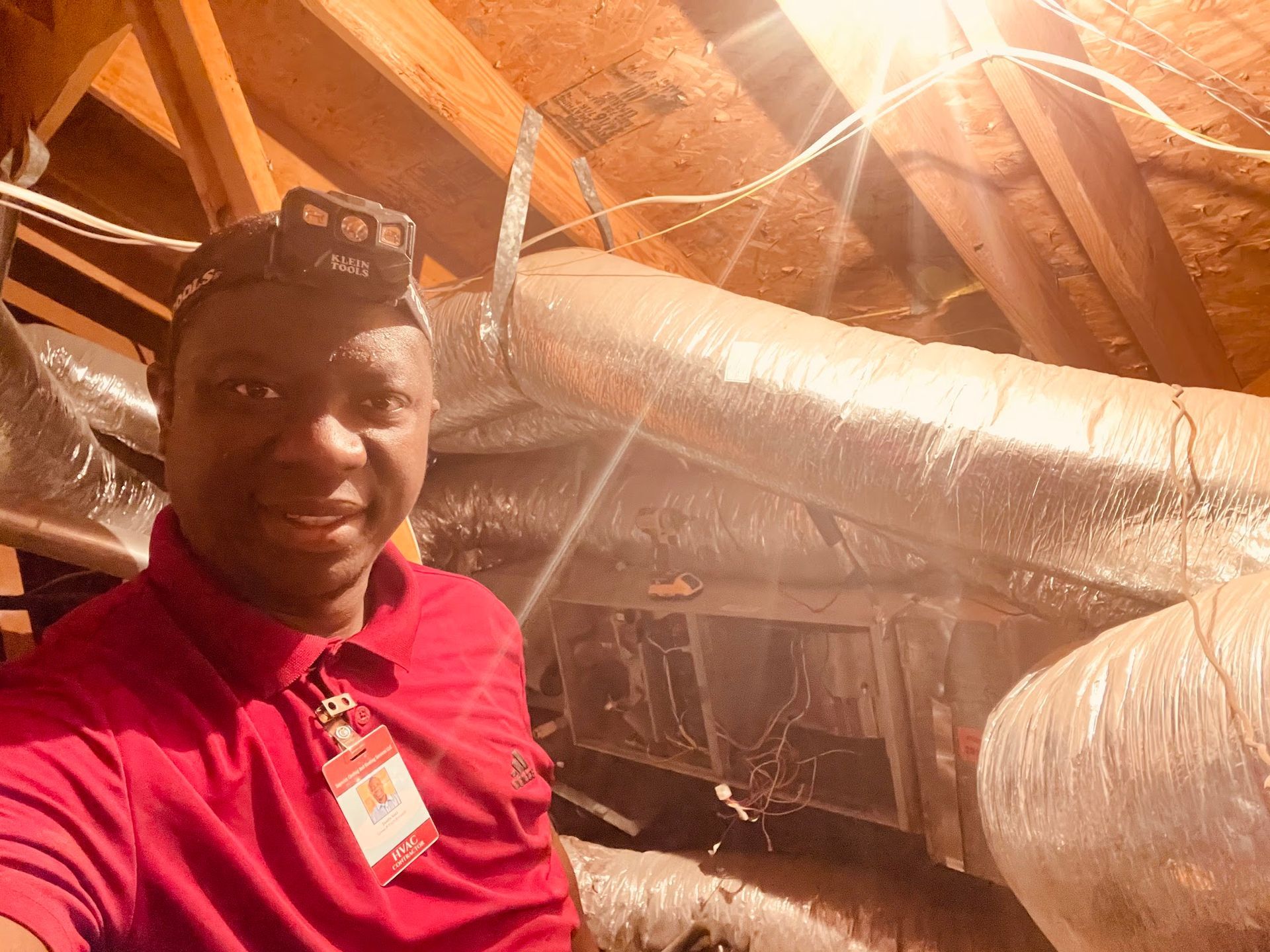 A man in a red shirt is taking a selfie in an attic.