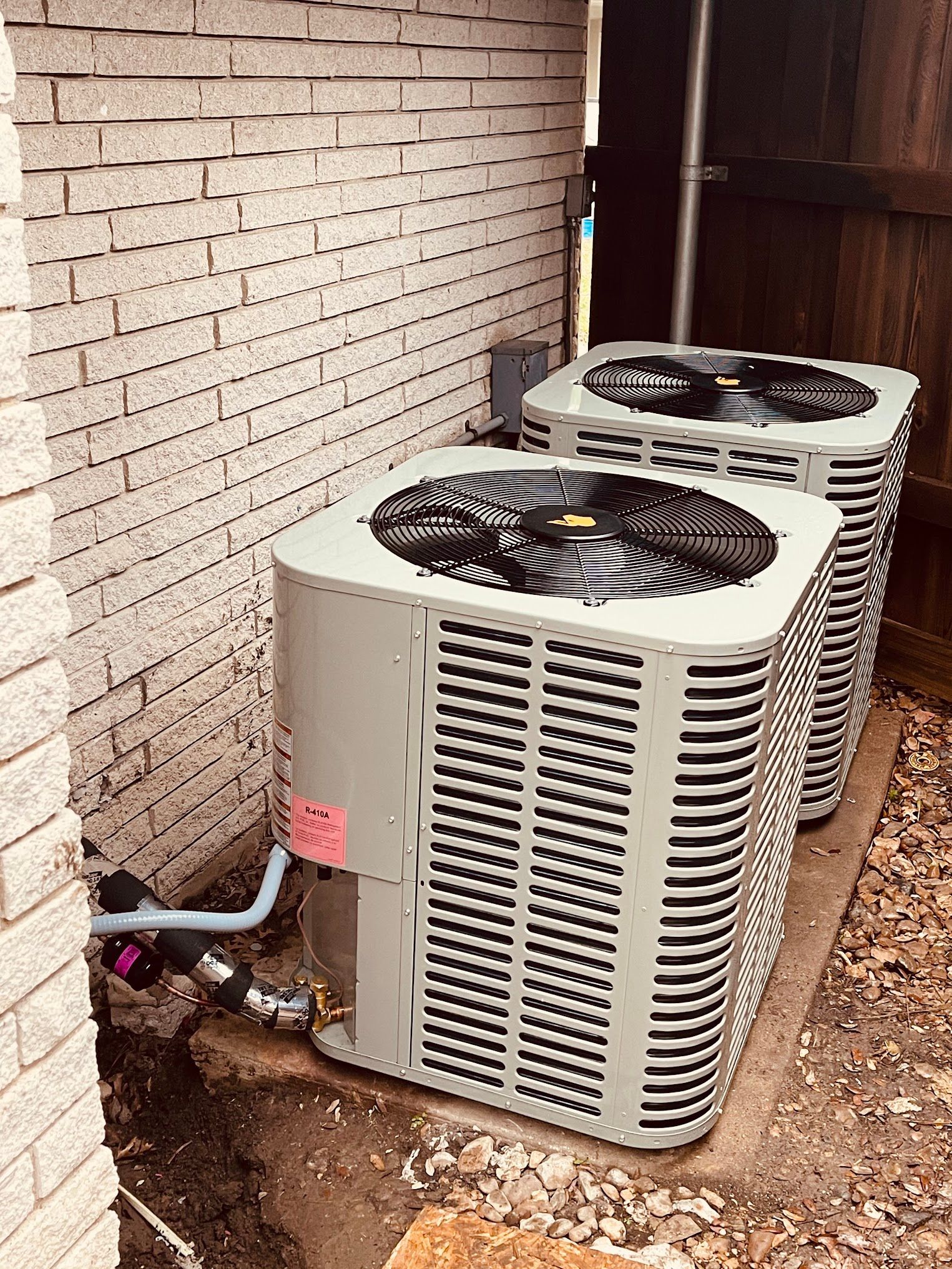 Two air conditioners are sitting next to each other on the side of a brick building.