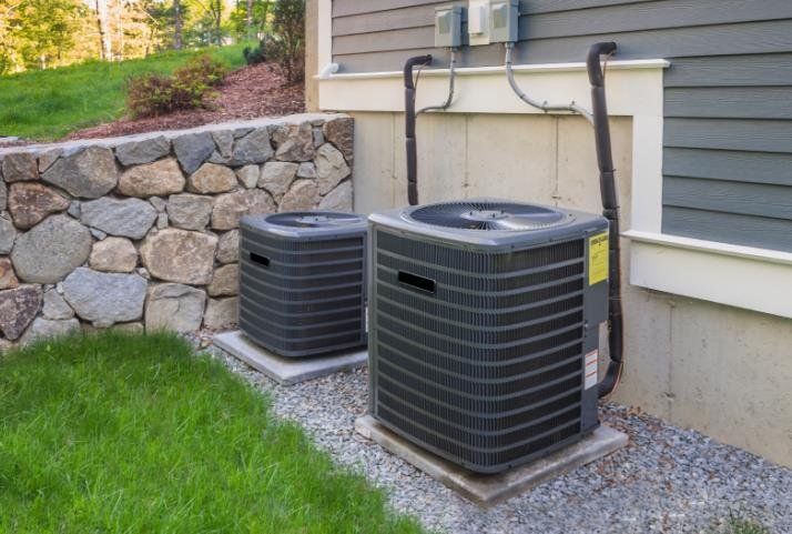 Two air conditioners are sitting on the side of a house.