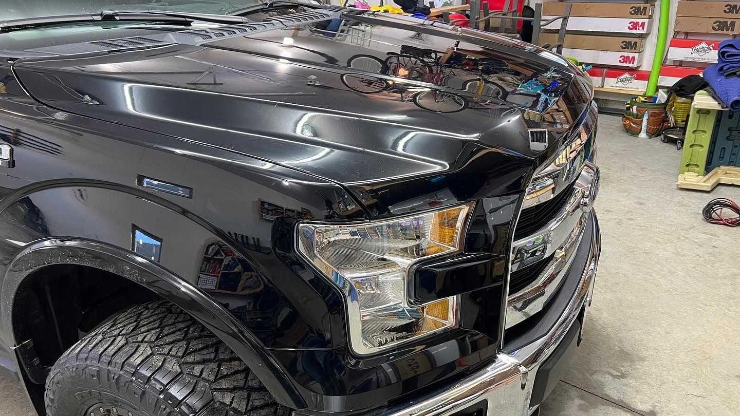 A black truck with the hood up is parked in a garage.
