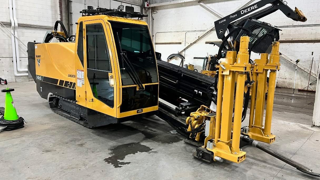 A yellow and black machine is sitting in a warehouse next to a green cone.