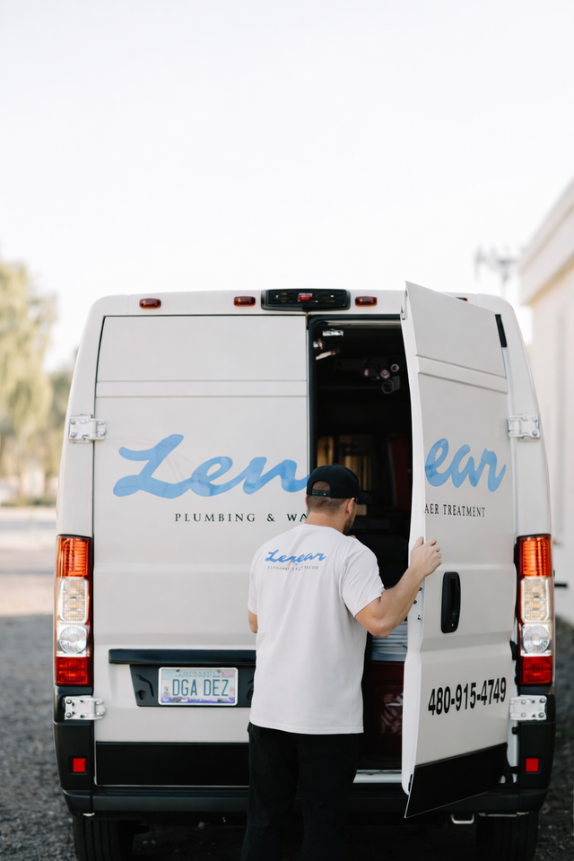 A person wearing a white logo t-shirt stands at the back of a white service van, loading equipment inside.