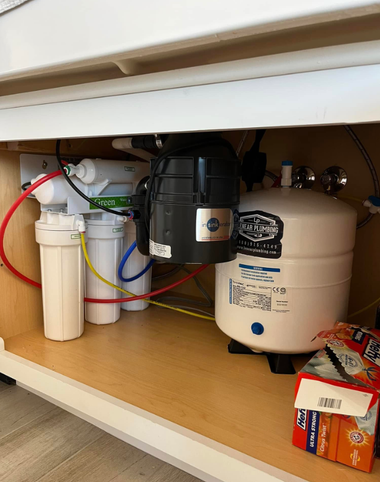 A multi-stage water filtration system with a white storage tank and various colored tubing installed under a kitchen sink.