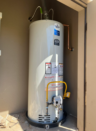 A vertical residential gas water heater with a yellow gas line, installed in a drain pan within a utility closet.