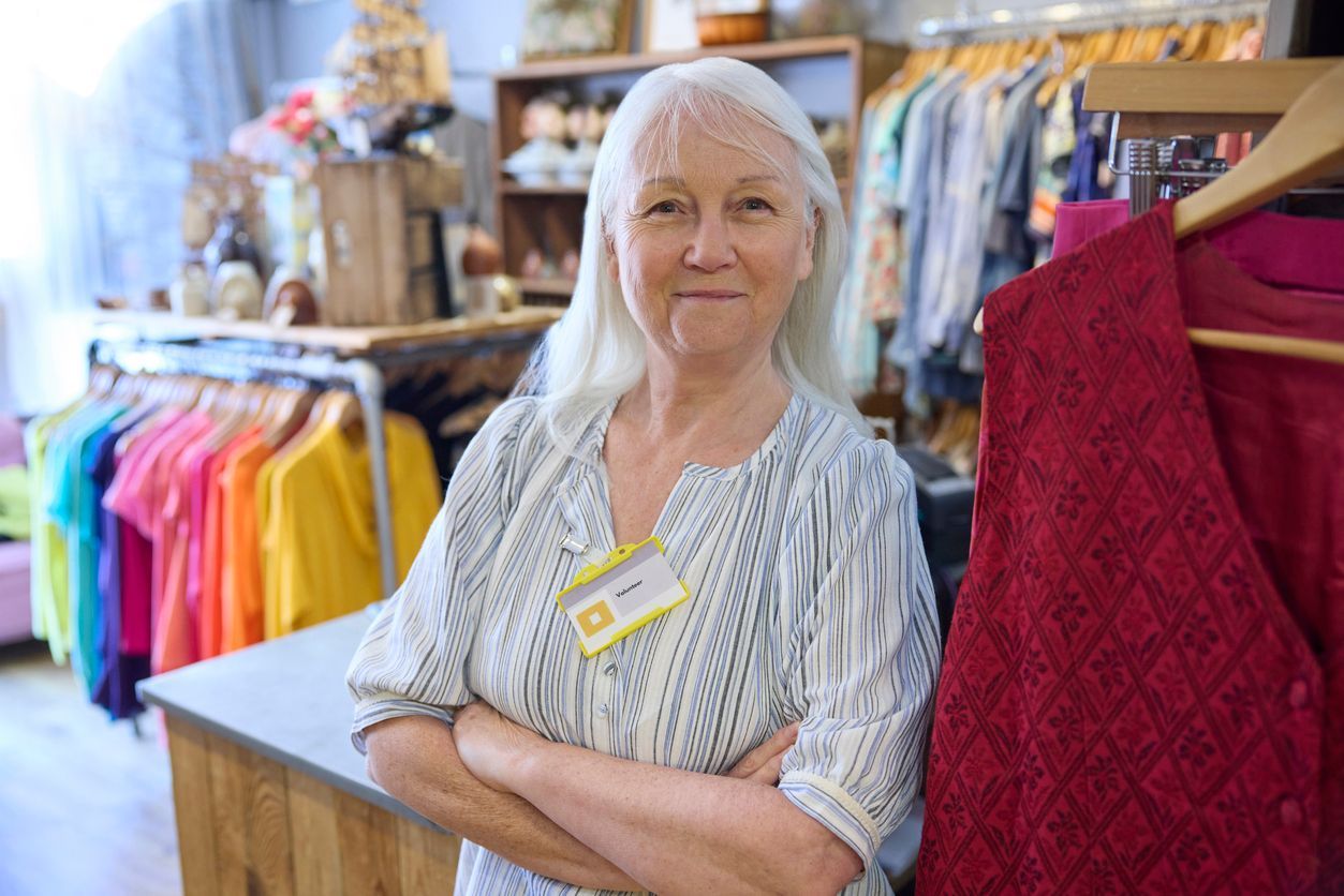 Retired senior volunteer smiling while helping customers at a charity shop in Dorset.
