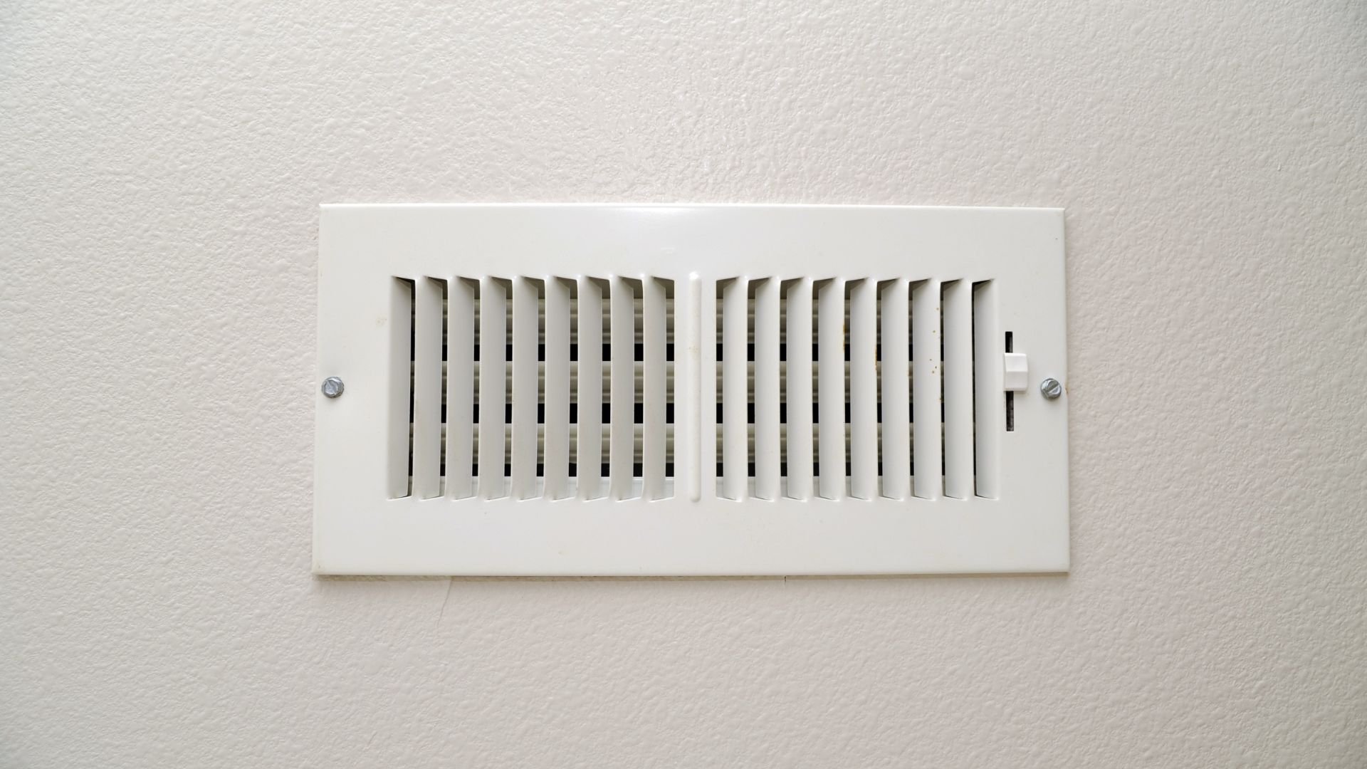 A vacuum hose is coming out of a hole in the floor next to a wooden vent.
