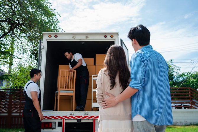 People loading boxes and a wooden chair into a moving truck outdoors
