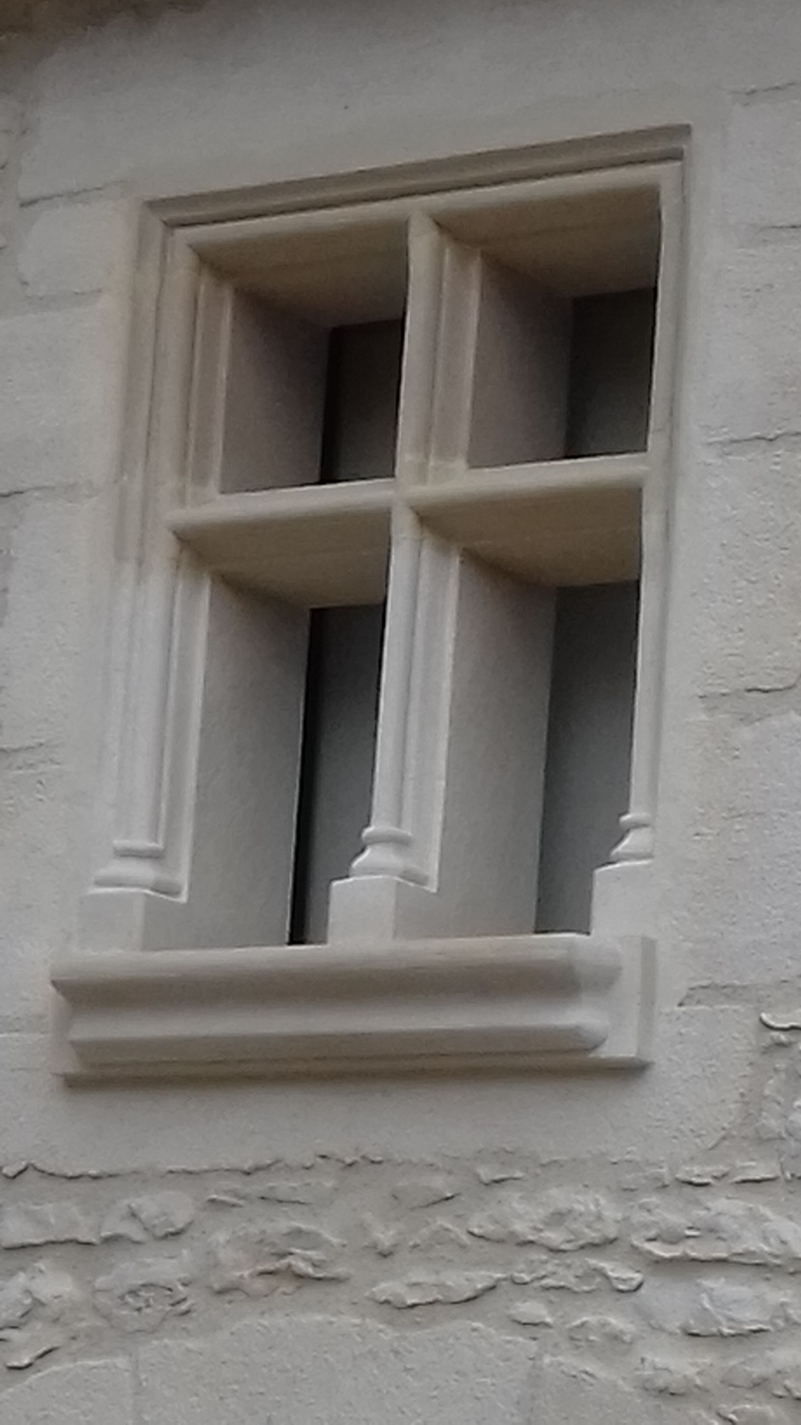 Petite fenêtre à cadre blanc et croisillons encastrée dans un mur en stuc clair
