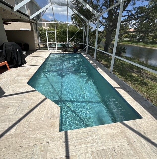 Pool cleaner being pulled out of a swimming pool by a person's hand. Blue water, tiles, and a white device.