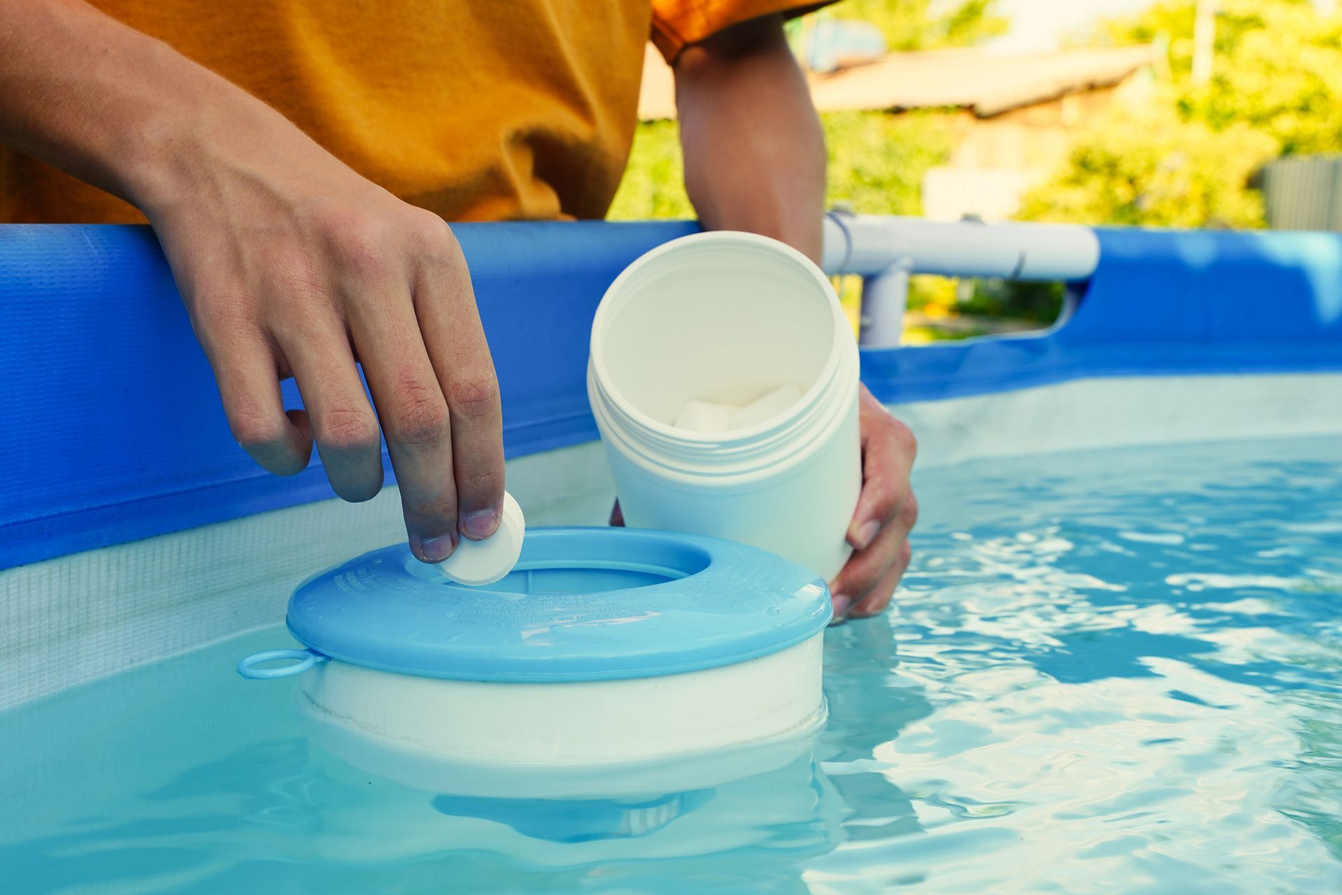 Person adding a chemical tablet to a floating pool chlorinator in a backyard pool.