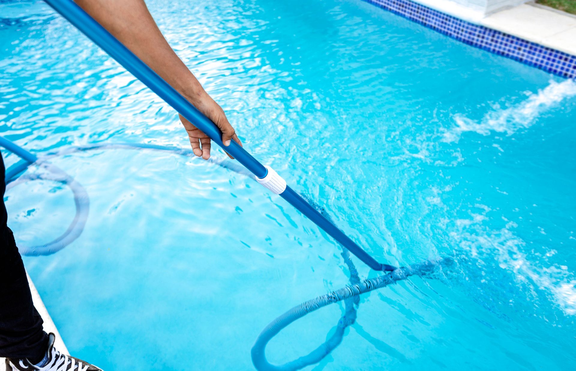 Person cleaning a blue swimming pool with a net and hose.